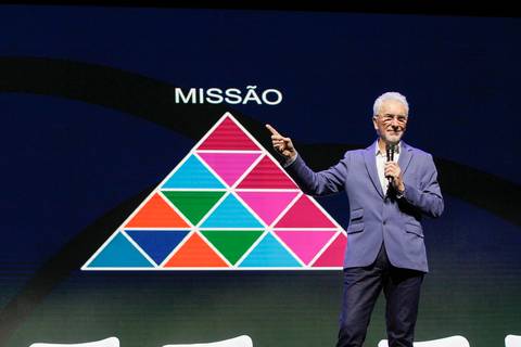 Eugenio Mussak, palestrante do Evento GPA, apontando para a palavra 'MISSÃO' em destaque no telão do Espaço Unimed em São Paulo, enfatizando um ponto crucial de sua palestra.'