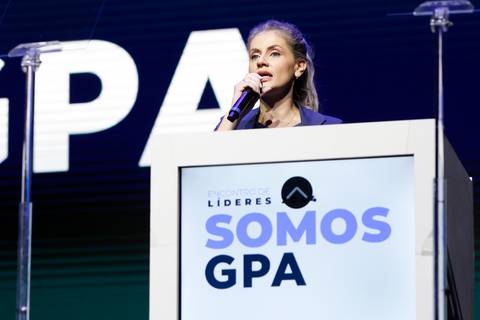 Apresentadora utilizando o púlpito com microfone no palco do Evento GPA no Espaço Unimed em São Paulo, dirigindo-se à plateia com clareza e dinamismo.'
