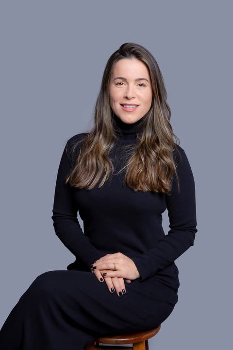 Jovem mulher em ensaio corporativo em São Paulo, sentada e vestindo preto, com as mãos cruzadas no colo, transmitindo uma postura profissional e confiante.'