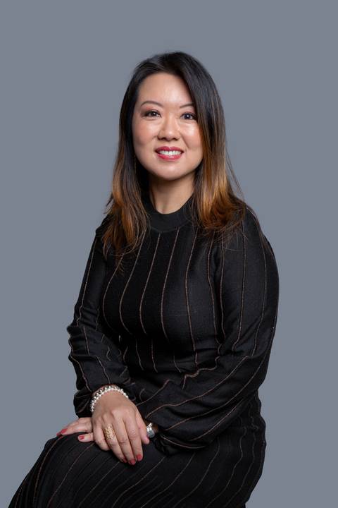 Mulher oriental de meia-idade, sentada em um ensaio corporativo em São Paulo, vestindo uma blusa preta de tecido elegante, exibindo sofisticação e profissionalismo.'