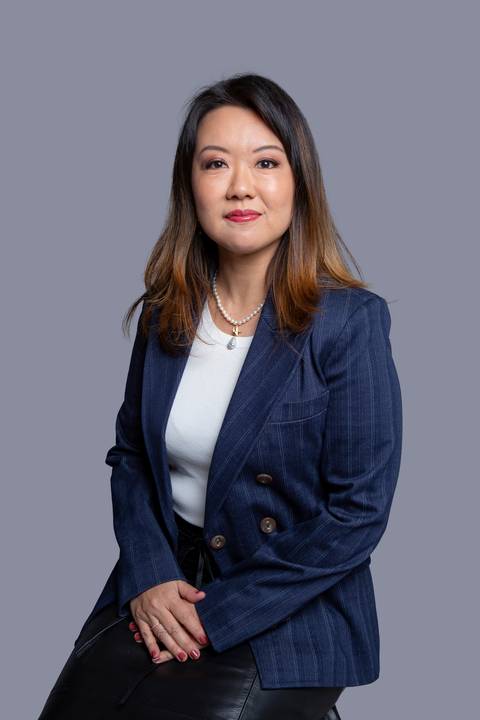 Mulher oriental de meia-idade, sentada em ensaio corporativo em São Paulo, vestindo um terno azul marinho listrado sobre uma blusa branca, com uma expressão séria e profissional'