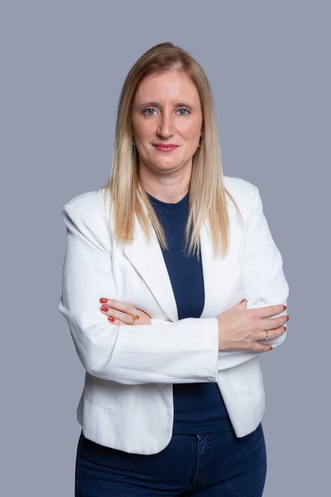 Mulher loira de pé, com os braços cruzados e olhar focado para frente, demonstrando postura executiva em ensaio corporativo em São Paulo/SP.'