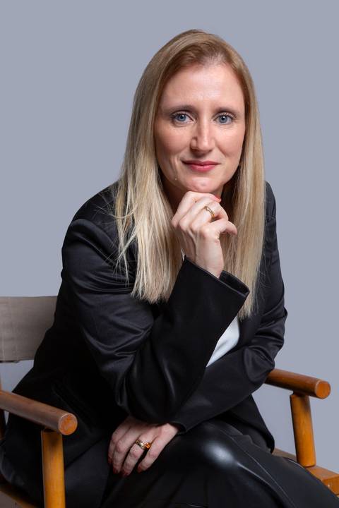 Mulher profissional sentada, usando blazer preto sobre blusa branca, segurando o queixo com os dedos em gesto reflexivo, em ensaio corporativo em São Paulo.'