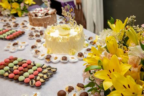 Mesa principal da festa de aniversário no Restaurante Nanako, São Paulo, ricamente decorada com bolos, uma variedade de docinhos finos e arranjos de flores frescas, criando um cenário convidativo.'