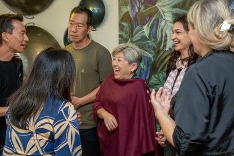 A aniversariante de 50 anos em um grupo de convidados, conversando e sorrindo abertamente, aproveitando a companhia e a festa no Restaurante Nanako em São Paulo.'