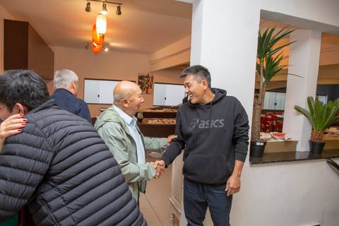 Um dos aniversariantes cumprimentando calorosamente um convidado, trocando sorrisos e gestos de afeto durante a festa no Restaurante Nanako em São Paulo.'