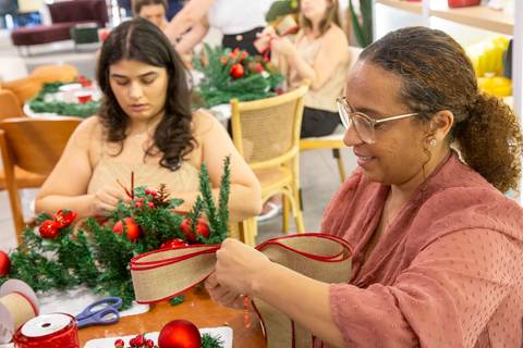 Participantes em processo de montagem de guirlanda natalina no Workshop da loja Westwing, em Moema. Registro que valoriza o fazer manual, a criatividade e o simbolismo natalino.'