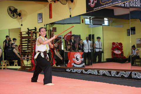 Participante do Exame de Faixa Preta na Academia Kwan Kun, em São Paulo, utilizando o bastão tradicional durante demonstração técnica. A imagem ressalta precisão, fluidez e domínio do corpo e da arma, simbolizando a tradição das artes marciais orientais.'