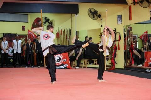Dois participantes em combate com bastões durante o Exame de Faixa Preta na Academia Kwan Kun, em São Paulo. A imagem captura a intensidade e a técnica do confronto, com foco no controle, respeito e domínio das armas tradicionais das artes marciais.'