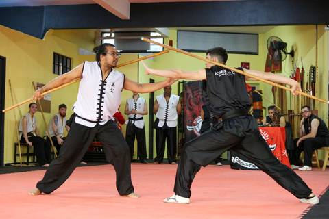 Participante do Exame de Faixa Preta em combate com mestre faixa preta usando bastão, na Academia Kwan Kun, em São Paulo. A imagem retrata o confronto técnico entre aluno e instrutor, simbolizando respeito, superação e aplicação prática da arte marcial.'