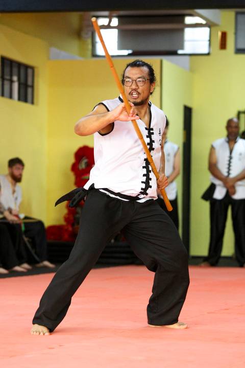 Close de participante do Exame de Faixa Preta na Academia Kwan Kun, em São Paulo, utilizando bastão com concentração e técnica. A imagem transmite foco, precisão e domínio nas artes marciais.'