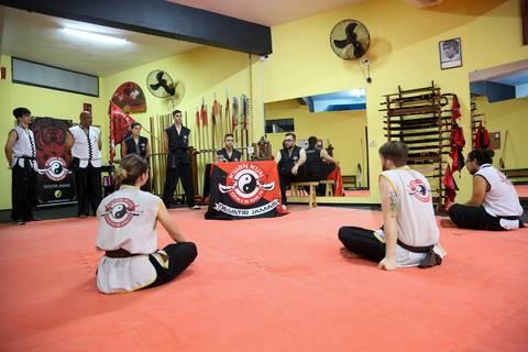 Participantes sentados ao redor da mesa do mestre durante o Exame de Faixa Preta na Academia Kwan Kun, em São Paulo. A imagem expressa respeito, escuta atenta e hierarquia marcial.'