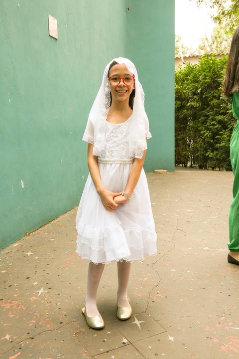 Criança menina vestindo a veste branca tradicional da catequese, sorrindo, em preparação para a Celebração Catequética na Paróquia Universitária Beato Carlo Acutis em São Paulo, simbolizando pureza e o rito religioso.'