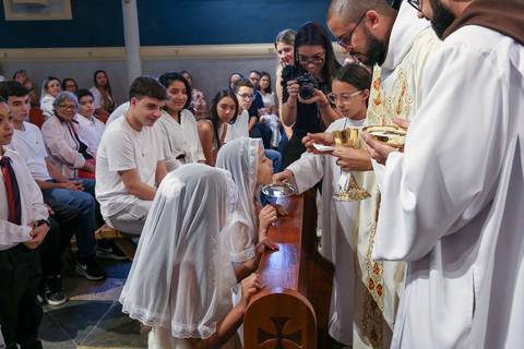 Crianças recebendo a Sagrada Eucaristia durante a Celebração Catequética na Paróquia Universitária Beato Carlo Acutis, em São Paulo. A imagem retrata a emoção do primeiro encontro com o Corpo de Cristo, em um gesto de fé, pureza e reverência, guiado pelo '