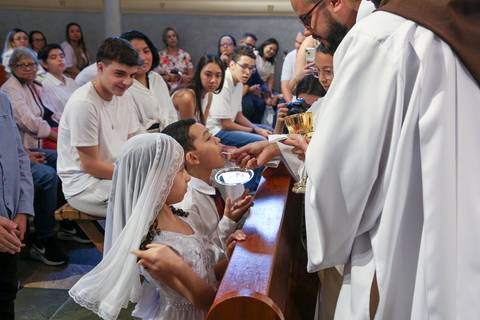 Crianças recebendo a Sagrada Eucaristia durante a Celebração Catequética na Paróquia Universitária Beato Carlo Acutis, em São Paulo. A imagem retrata a emoção do primeiro encontro com o Corpo de Cristo, em um gesto de fé, pureza e reverência, guiado pelo '