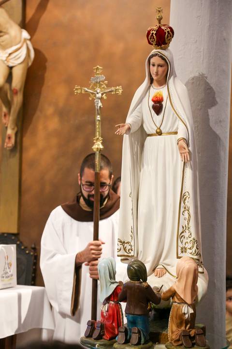 Frei ao fundo da cena segurando o bastão pastoral durante a Celebração Catequética na Paróquia Universitária Beato Carlo Acutis, em São Paulo. A imagem destaca a presença silenciosa da autoridade espiritual, com o báculo simbolizando o pastoreio e a missã'