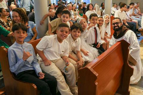Grupo de crianças catequizandas, vestidas com suas vestes brancas, posando alegremente para uma foto no ambiente da Paróquia Universitária Beato Carlo Acutis em São Paulo, celebrando o momento da Celebração Catequética.'