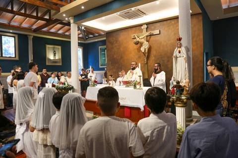 Momento solene da Celebração Catequética na Paróquia Universitária Beato Carlo Acutis em São Paulo, com o padre proclamando a Palavra durante a homilia. A imagem destaca a expressão do celebrante, o ambão decorado e a atenção dos fiéis, transmitindo espir'