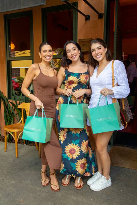 Influenciadores digitais sorridentes posando com as sacolas personalizadas da Westwing durante o evento exclusivo no Clandestina Restaurante em São Paulo, exibindo os brindes e a parceria entre a marca e os criadores de conteúdo.'