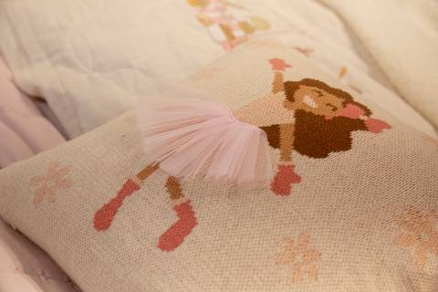 Plano detalhe de travesseiro decorativo da Karsten no estande da ABUP Show 2025 no Distrito Anhembi, exibindo estampa com imagem de menina e saia, destacando o design e a linha de produtos para cama'