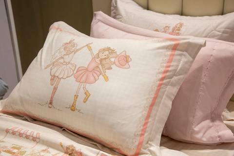 Plano detalhe de travesseiro decorativo da Karsten no estande da ABUP Show 2025 no Distrito Anhembi, exibindo estampa com imagem de duas meninas, destacando o design e a linha de produtos para cama'