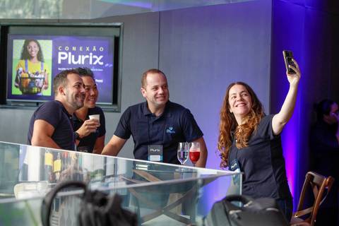 Grupo de participantes sorridentes tirando uma selfie animada no evento corporativo da Plurix no Teatro B32 em São Paulo, capturando momentos de descontração e networking'