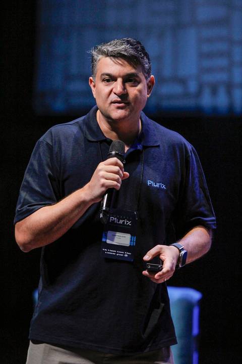 CEO da Plurix palestrando no palco do Teatro B32 em São Paulo, durante evento corporativo, com projeção ao fundo e foco na liderança'