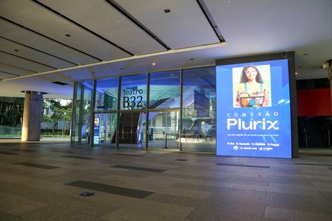Entrada do Teatro B32 em São Paulo, com um painel visível da empresa Plurix, destacando a parceria e o local do evento corporativo'