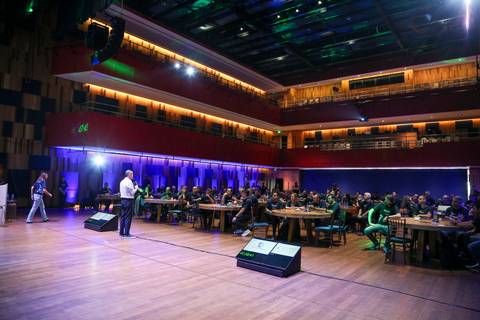 Plano aberto do palco do Teatro B32 em São Paulo durante a apresentação no evento corporativo da Plurix, com palestrante e cenário iluminados e a atenção da plateia'