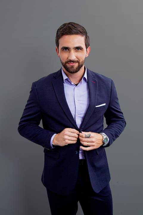 Retrato corporativo de homem de negócios de pé, segurando o botão de seu terno azul marinho com as duas mãos, em fundo cinza profissional'