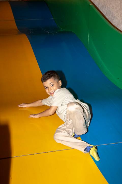Menino aniversariante comemorando, deslizando sorridente por um grande escorregador colorido no Kid Recanto Buffet em São Paulo, em festa de aniversário infantil'