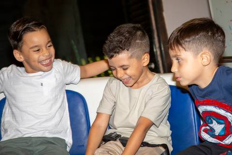Menino aniversariante sorrindo com dois amigos em brinquedo de centrifugação (rotor) que gira e prende por cinto no Kid Recanto Buffet em São Paulo, em momento de pura diversão na festa infantil'