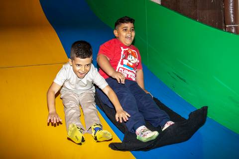 Menino aniversariante e amigo descendo juntos e sorrindo por um escorregador colorido grande no Kid Recanto Buffet em São Paulo, compartilhando a diversão na festa de aniversário infantil'