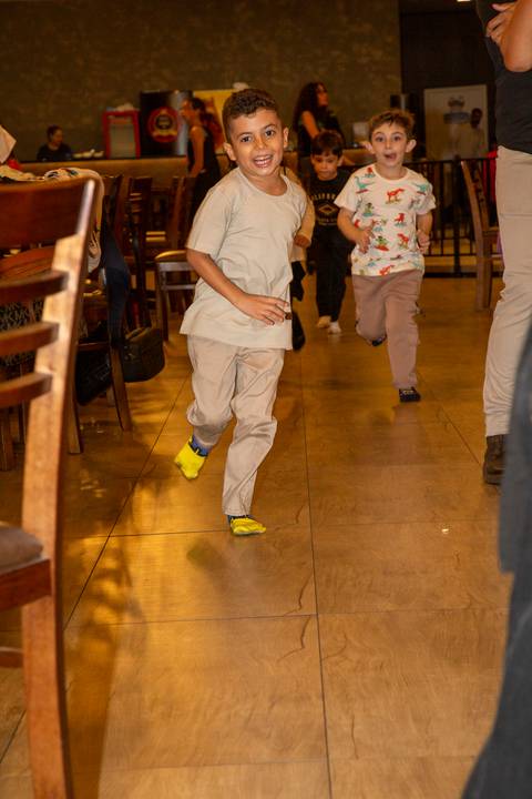 Menino aniversariante correndo descalço (apenas de meia) e sorrindo no Kid Recanto Buffet em São Paulo, aproveitando a liberdade da festa infantil colorida e animada'