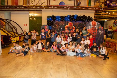 Crianças convidadas sorrindo e posando em frente ao bolo de aniversário temático do Homem-Aranha, no cenário vibrante do Kid Recanto Buffet em São Paulo'