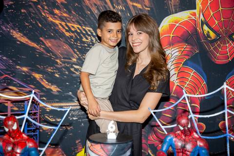 Menino aniversariante sorrindo ao posar com a tia atrás do bolo de aniversário com decoração temática do Homem-Aranha no Kid Recanto Buffet em São Paulo, em celebração dos seus 6 anos'