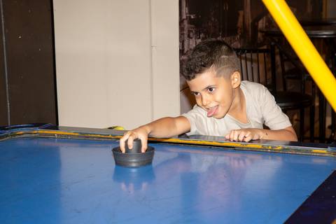 Menino aniversariante concentrado jogando Air Hockey, tentando fazer gol com o disco de ar no Kid Recanto Buffet em São Paulo, em momento de diversão na festa infantil'
