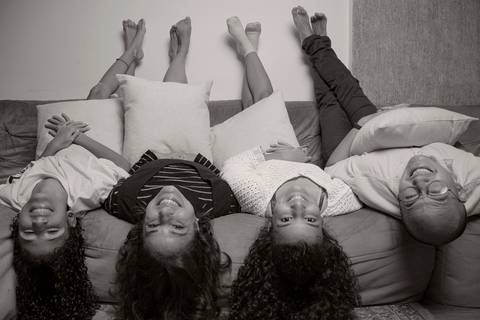 Foto em preto e branco de família deitada no sofá de cabeça para baixo com os pés na parede, com as duas filhas, mãe e pai em sequência, em uma pose divertida e acrobática em ensaio de família em SP'