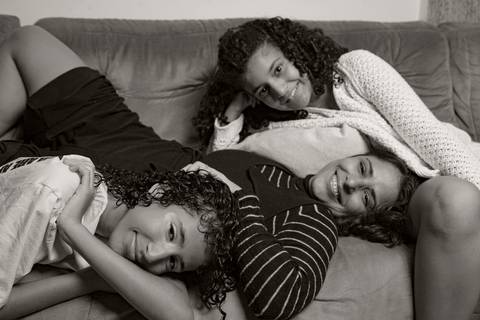 Foto em preto e branco de mãe deitada no colo de uma filha no sofá, com a outra filha também deitada à frente, em um momento íntimo e relaxante em família em ensaio de família em SP'