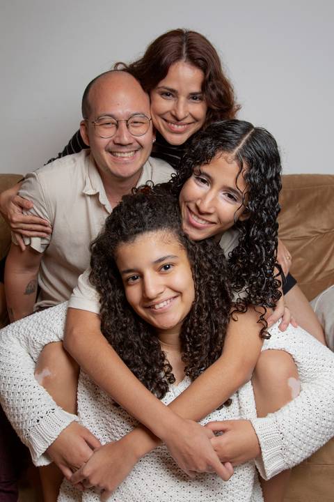 Retrato familiar para ensaio Dia das Mães 2025, com mãe posicionada acima, pai logo abaixo, e filhas abraçadas com uma abaixo do sofá, em uma composição afetuosa em ensaio de família em SP'