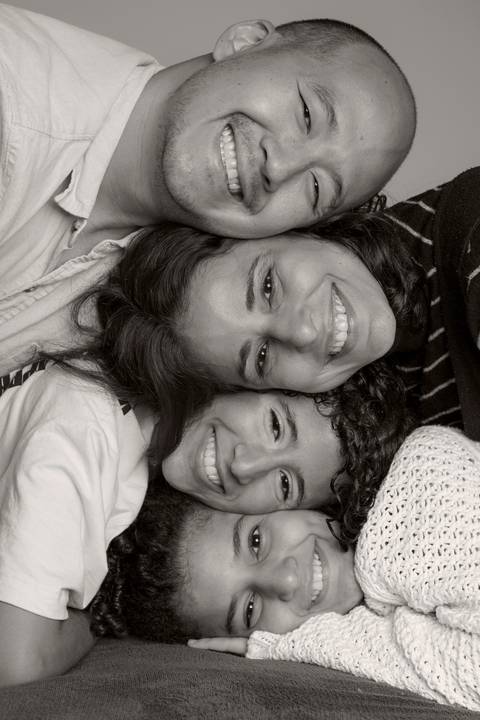 Foto em preto e branco de família amontoada, com as cabeças em arranjo vertical, pai no topo, seguido pela mãe e pelas filhas, transmitindo união e afeto em ensaio de família em SP'