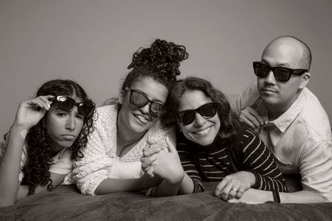 Foto em preto e branco de família deitada na cama, com as duas filhas, mãe e pai em sequência, todos usando óculos escuros, em um momento descontraído e divertido em ensaio de família em SP'
