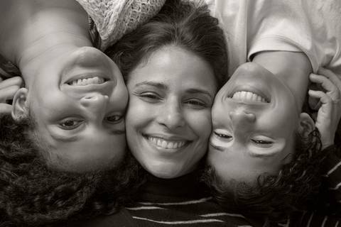 Foto em preto e branco de mãe no centro deitada com as duas filhas, uma de cada lado também deitadas com as cabeças invertidas, em uma pose divertida e criativa de família em ensaio de família em SP'