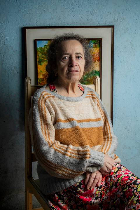 Retrato de mãe com iluminação de luz dura, em frente a uma parede azul com um quadro decorativo ao fundo em ensaio de família em Mauá'