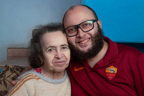 Mãe e filho sentados juntos em um sofá confortável, com uma parede azul ao fundo, em um momento de união em ensaio de família em Mauá'