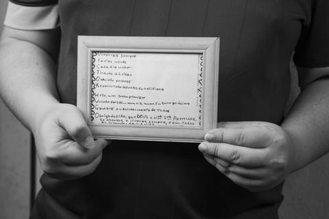Foto em preto e branco em close-up de um acróstico emoldurado, presente tocante feito pelo falecido pai, sendo segurado pelas mãos do filho, evocando memória e saudade em ensaio de família em Mauá'