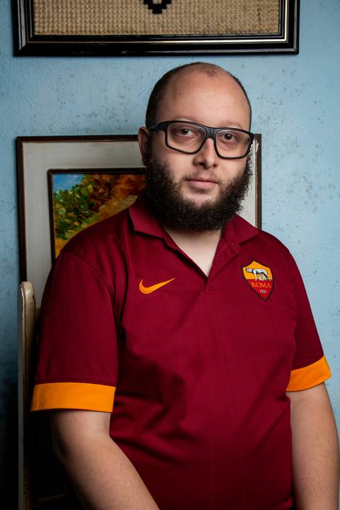 Retrato de filho com iluminação de luz suave, em frente a uma parede azul com um quadro decorativo ao fundo em ensaio de família em Mauá'