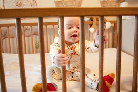 Bebê no berço brincando, segurando as grades com as mãos, em um momento de descoberta em ensaio de família em SP'