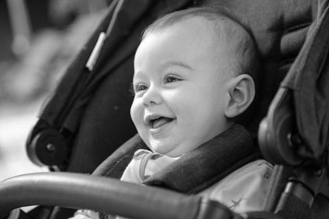 Foto em preto e branco de bebê sorrindo feliz no carrinho de bebê, com foco no rosto em ensaio de família em SP'