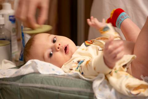 Bebê deitado em trocador enquanto um adulto troca sua fralda em ensaio de família em SP'